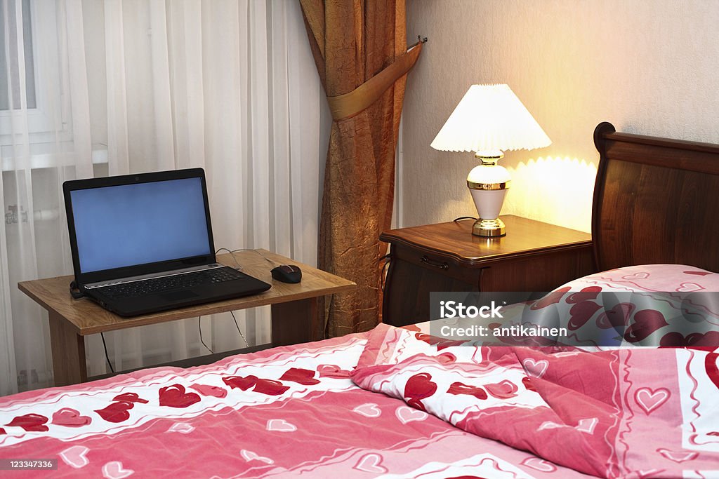Computadora portátil en la mesa cerca de cama - Foto de stock de A la moda libre de derechos