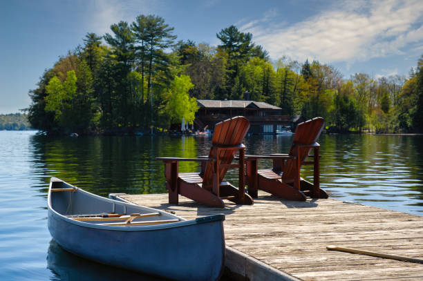 Canoe tied to a dock with Muskoka chairs stock photo