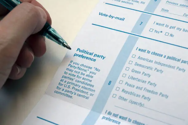 Closeup of a 'Political Party Preference' section on a Voter Registration form, and a hand holding pen next to it