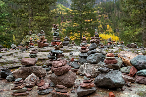 Horizontal photograph of multiple stacks of balancing rocks sitting high on a mountain trail in Telluride Colorado. A beautiful mountain range is out of focus in the background.