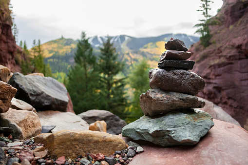Horizontal photograph of a stack of balancing rocks sitting high on a mountain trail in Telluride Colorado. A beautiful mountain range is out of focus in the background.