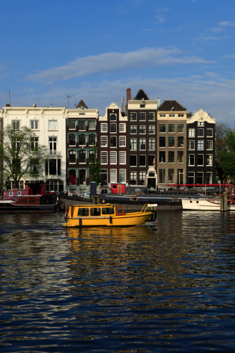 yellow water taxi passing characteristic facades and gables of Amsterdam' canal houses; Amsterdam, Netherlands