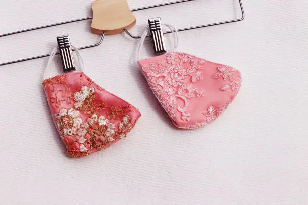 Photo of Pink lace reusable face masks hanging on clothes hanger placed on white background.