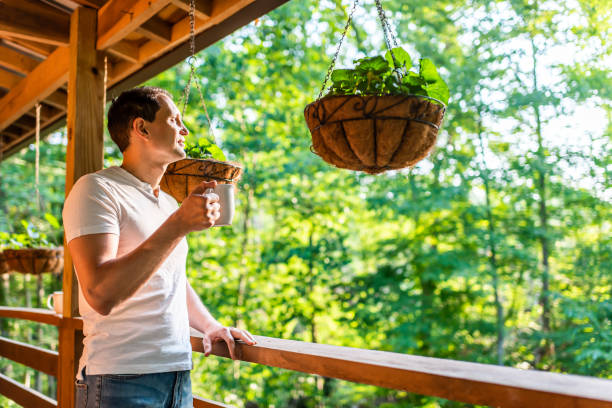 Hanging potted plant flowerpot with man drinking coffee tea mug cup on porch of log cabin cottage house with green color Hanging potted plant flowerpot with man drinking coffee tea mug cup on porch of log cabin cottage house with green color drinks on the deck stock pictures, royalty-free photos & images