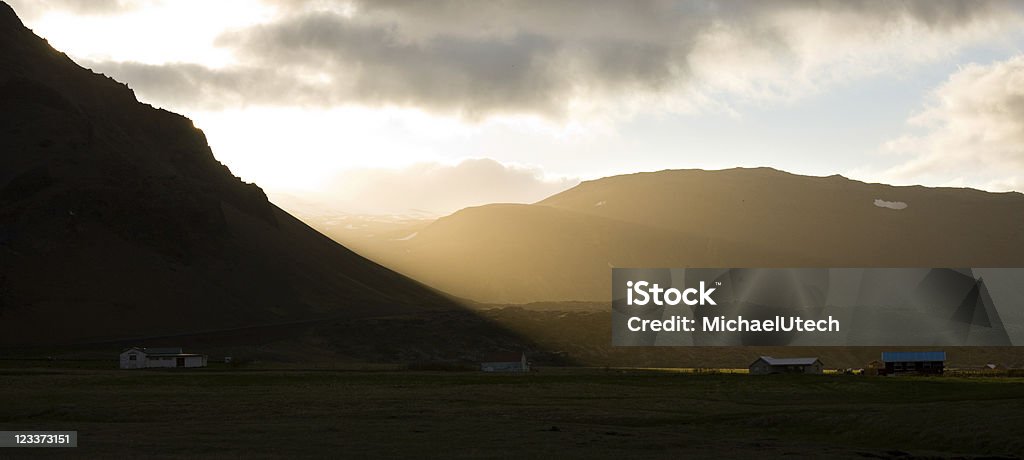 Evening In Arnarstapi, Iceland Beautiful evening light with the sun shining between clouds and mountain, the village of Arnarstapi in the foreground. Arnarstapi Stock Photo