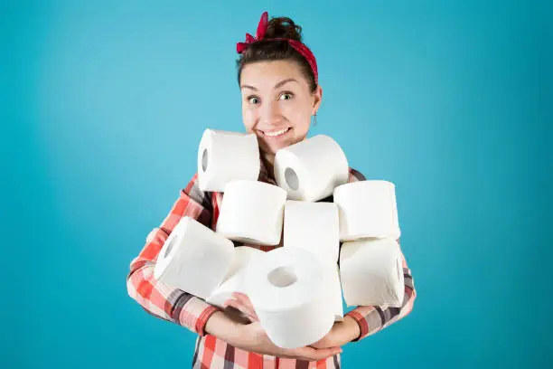 Smiling joyful girl holds an armful of toilet paper rolls on a blue background