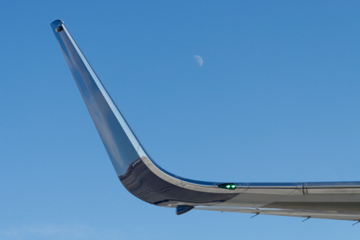 Winglet of a Boeing 757 against a blue sky with a half-moon in the background.