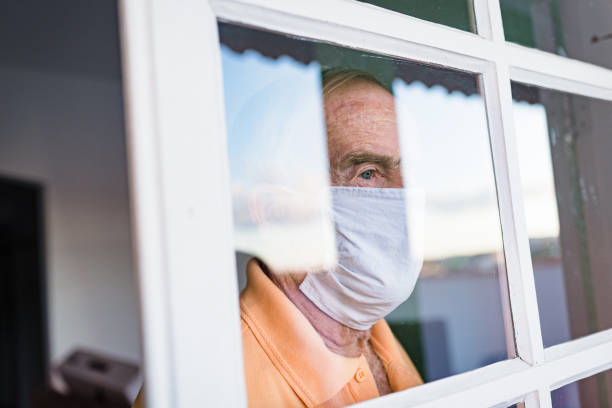 istock Covid-19: Senior man in mask looking out of window 1233856816