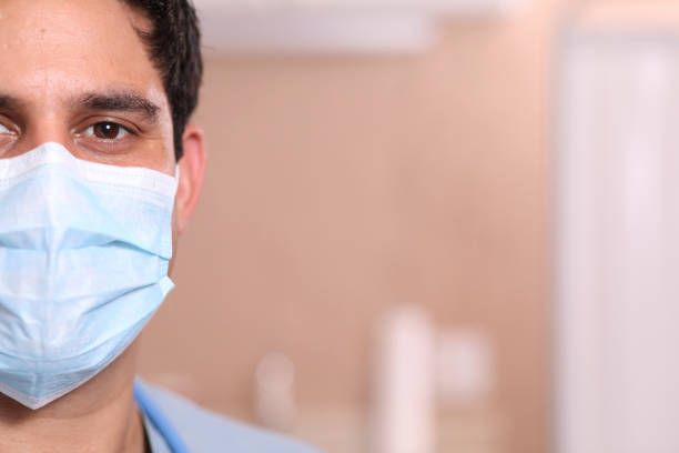 Latin descent doctor or healthcare worker wearing his protective face mask during work in hospital or clinic setting.  Coronavirus, medical exam, consultation.  Close up, half face.