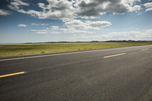 Beautiful idyllic landscape in countryside banner format with a wide field of cereals and a pasture divided by a deserted asphalt road against a blue summer sky.