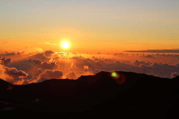 an incredible sunrise as the sun crests over the cloud covered haleakala crater in haleakala national park in maui, hawaii - haleakala crater imagens e fotografias de stock