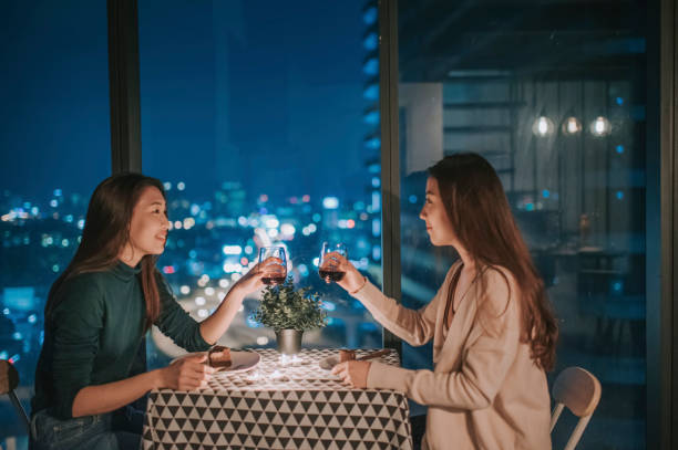 an LGBT couple enjoying their drink with city view at background at night on candlelight date an LGBT couple enjoying their red wine with city view at background at night on candlelight date gay dinner table stock pictures, royalty-free photos & images