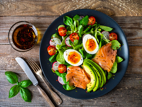 Smoked salmon with boiled eggs, avocado and vegetables on wooden table