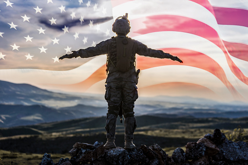 Silhouette of soldier against sunset sky with American flag