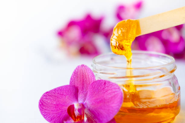 istock sugar paste or wax honey for hair removing flows down from wooden waxing spatula sticks. flower background - depilation and beauty concept 1234443448