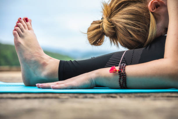 Close-up of a woman practicing yoga in seated forward bend pose (Paschimottanasana).