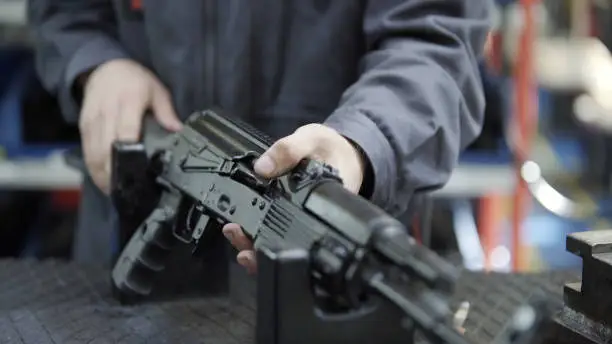 Photo of Factory assembly of a Kalashnikov assault rifle. Close up of charging rifle. AK47 loading. Factory worker hand charging machine gun. Factory worker collects the AK-47.