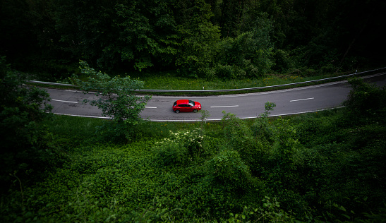 Germany, Bavaria. A red car drives through a forested road.