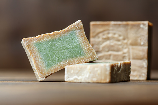 Bar and two slices of traditional aleppo organic laurel soap on a brown wooden background. Skin treatment concept