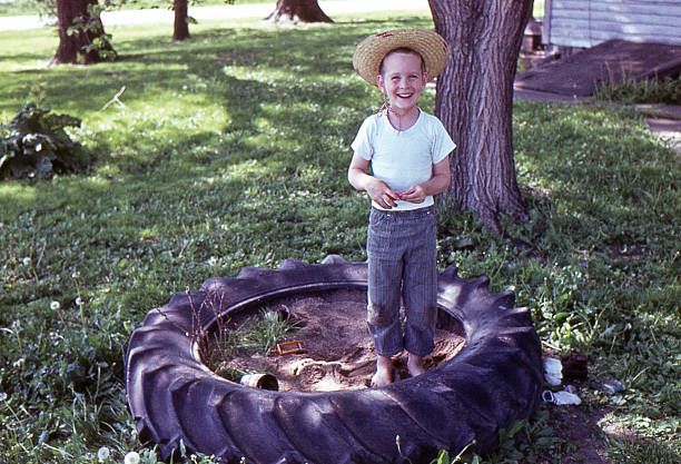boy in sandbox 1964, retro Little boy in tractor tire sandbox. Iowa, USA 1964. Agfachrome scanned film with grain. sandbox photos stock pictures, royalty-free photos & images