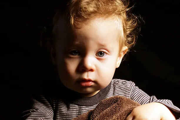 Low key image of blond one year old toddler with brown blanket.