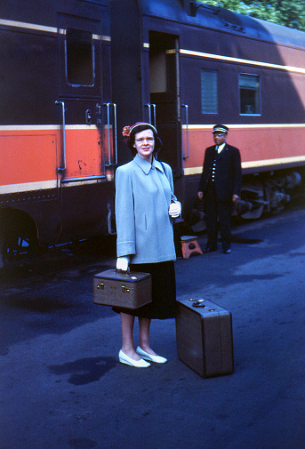 Woman with suitcases boarding passenger train. Iowa, USA, 1951. Kodachrome scanned film with grain.