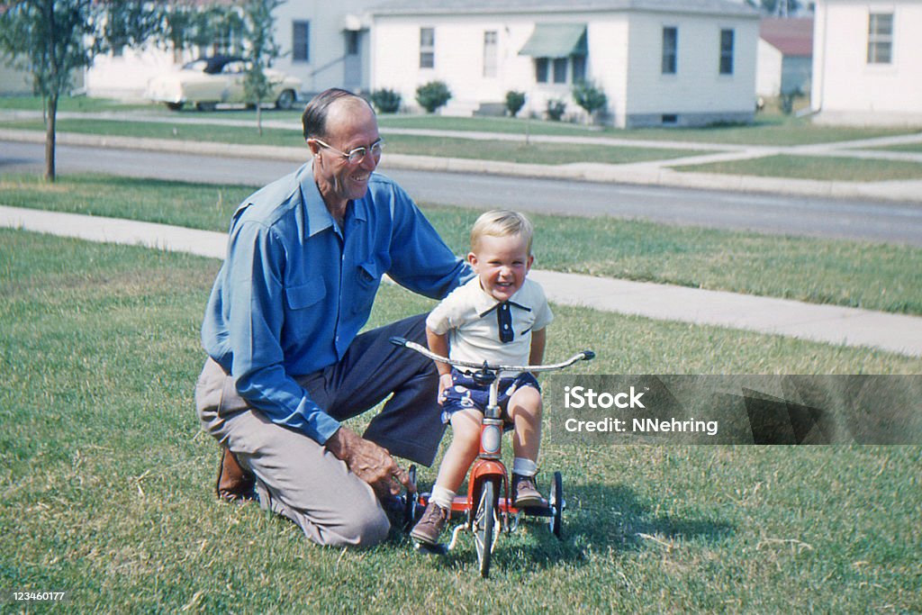 grandfather teaching grandson to ride tricycle 1953, retro Grandfather helping grandson learn to ride tricycle. Iowa, USA 1953. Kodachrome scanned film with grain. Photograph Stock Photo