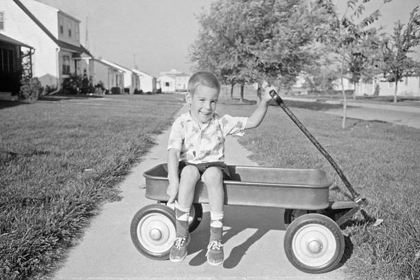boy in wagon 1957, retro Little boy sitting in wagon in his front yard. 1957, Waterloo, Iowa, USA. Scanned film with grain. iowa photos stock pictures, royalty-free photos & images