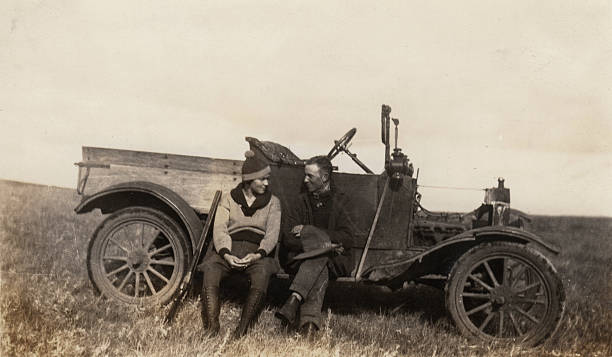 Photo taken 1920. Romantic couple on a bird hunting trip, resting on the side of an old car. 