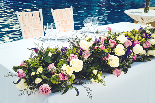 Newlyweds table at the wedding reception dinner decorated with flowers. Tropical location, resort wedding concept. Toned image with place for text