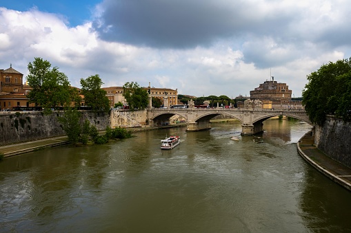 Rome, Italy, May 8, 2018: A ship sails down the Tiber River. In the background is the Ponte Vittorio Emanuele II. and the Castel Sant'Angelo.
