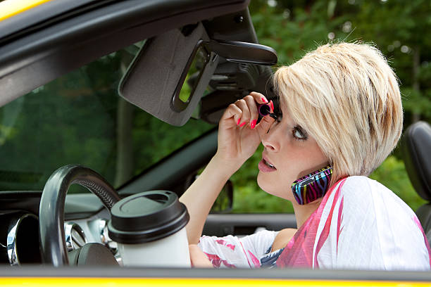 Dangerous Driving Young woman applying makeup, talking on the phone and drinking coffee while driving. Seatbelt not attached. careless stock pictures, royalty-free photos & images