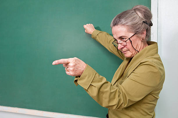 stricte enseignant pointant sur étudiant - professor teacher female blackboard photos et images de collection