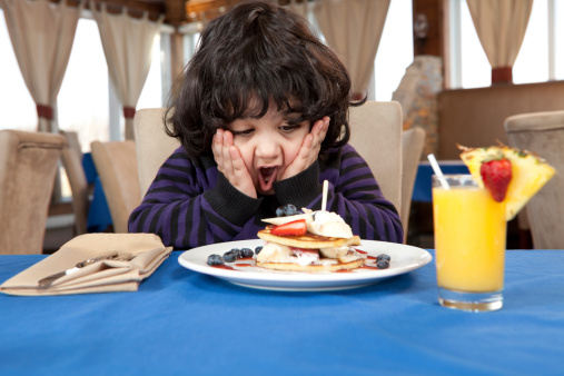 Ecstatic young boy eating a stack of pancakes for breakfast at a family restaurant