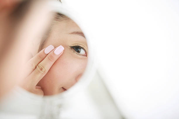 young woman looking at self in mirror,skin care - pampering ストックフォトと画像