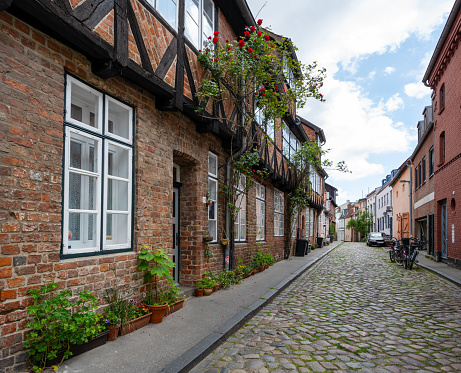 Typical narrow alley with residential buildings and pottet flowers on the sidewalk garden in the old town of the hanseatic city Luebeck, Germany