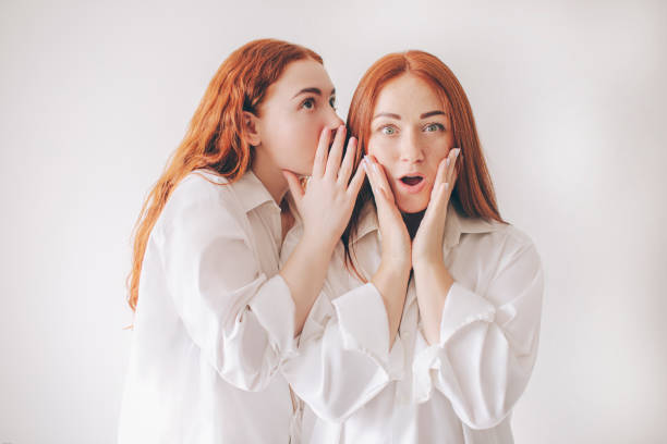 istock Two red-haired sisters stand isolated on a white background in spacious oversized shirts. Two young women gossip about someone. 1234708809
