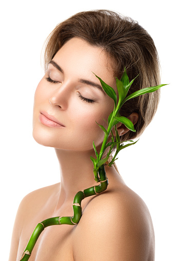 Portrait of young beautiful woman with a green bamboo branch on white background