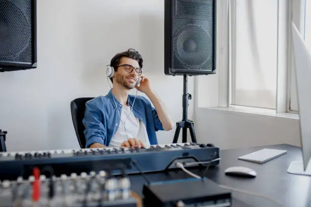 Photo of Male music arranger composing song on midi piano and audio equipment in digital recording studio. Man produce electronic soundtrack or track in project at home.