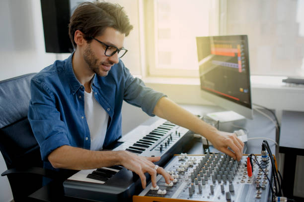istock music producer is composing a song on synthesizer keyboard and computer in recording studio. Man is working on sound mixer in recording studio or DJ is working in broadcasting studio 1234728031