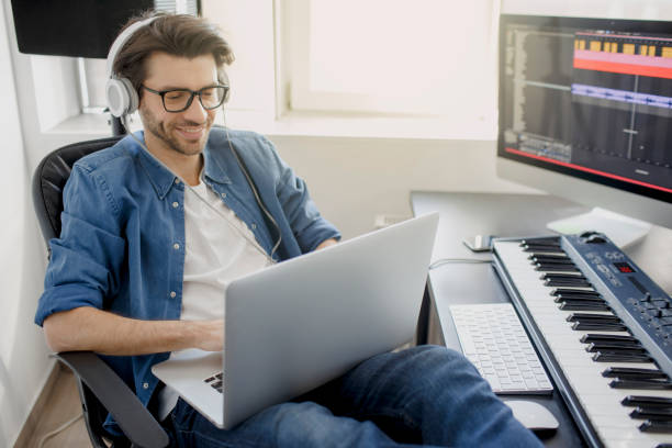 istock Working on a laptop. Busy guy. Multitasking concept. DJ in broadcasting studio. music producer is composing a song on synthesizer keyboard and computer in recording studio. 1234730604