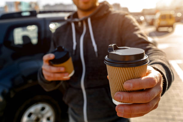Disposable paper cup with hot drink. A man drinks coffee or tea and offers to share a drink with you!