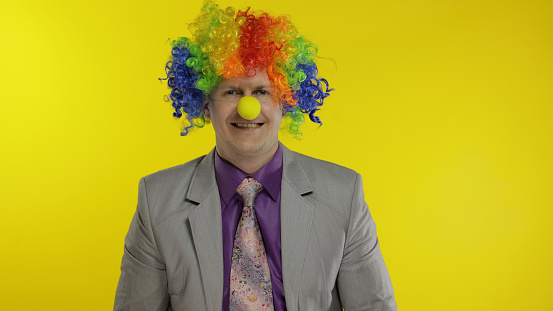 Successful clown manager office worker in wig and business suit at work. Guy businessman entrepreneur boss smiles, looks at camera. Copy space. Halloween. Yellow background