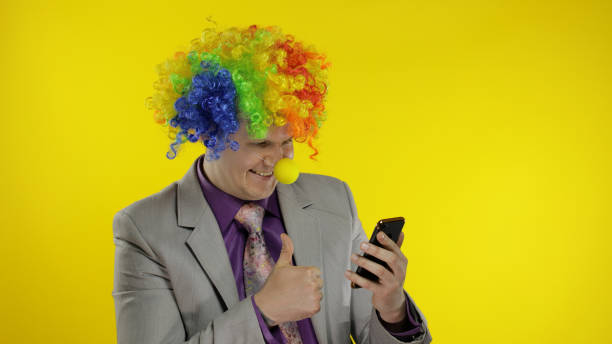 клоун бизнесмен предприниматель в парике с помощью приложения на смартфоне для работы в интернете - clown circus telephone humor стоковые фото и изображения