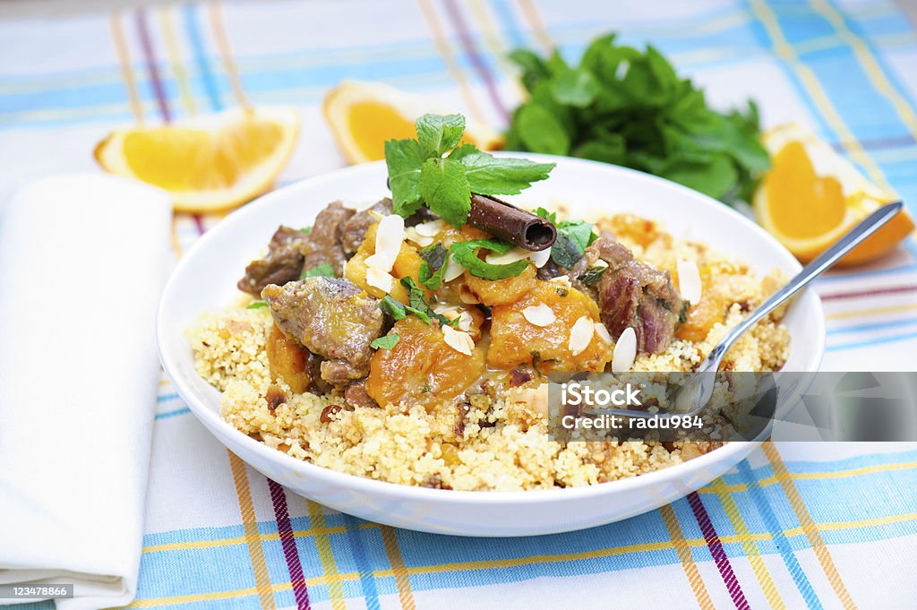 Lamb Couscous A plate with delicious looking cous cous with lamb meat, apricots, almonds, raisins, dates, cinnamon and mint. I used some mint leaves and orange slices in the background. Apricot Stock Photo