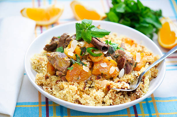Moroccan Lamb and Apricot Couscous A plate with delicious looking couscous with lamb meat, apricots, almonds, raisins, dates, cinnamon and mint. I used some mint leaves and orange slices in the background. couscous stock pictures, royalty-free photos & images