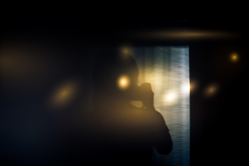silhouette of  person holding camera in semi-darkness with sun flare in dark room in front of window