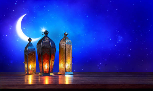 Ramadan lanterns on the table with moon on dark blue background. Beautiful Greeting Card with copy space for Muslim Holidays. An illuminated Arabic lamp. Mixed media. stock photo