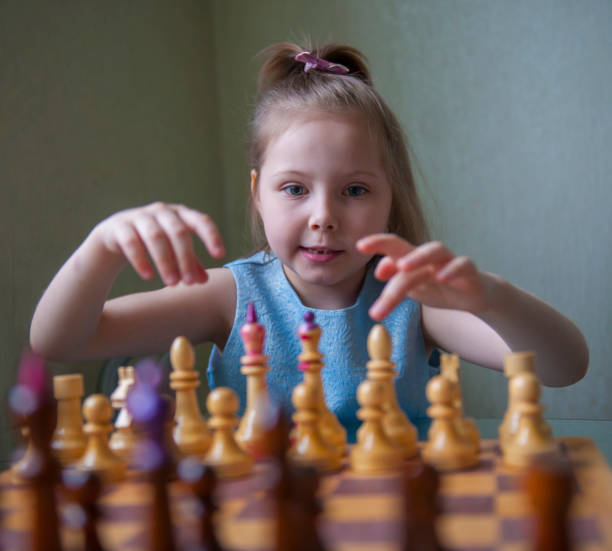 une fillette de cinq ans apprend à jouer aux échecs. - board game piece leisure games blue isolated photos et images de collection