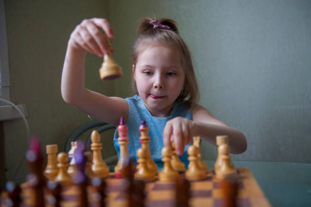 une fillette de cinq ans apprend à jouer aux échecs. - board game piece leisure games blue isolated photos et images de collection